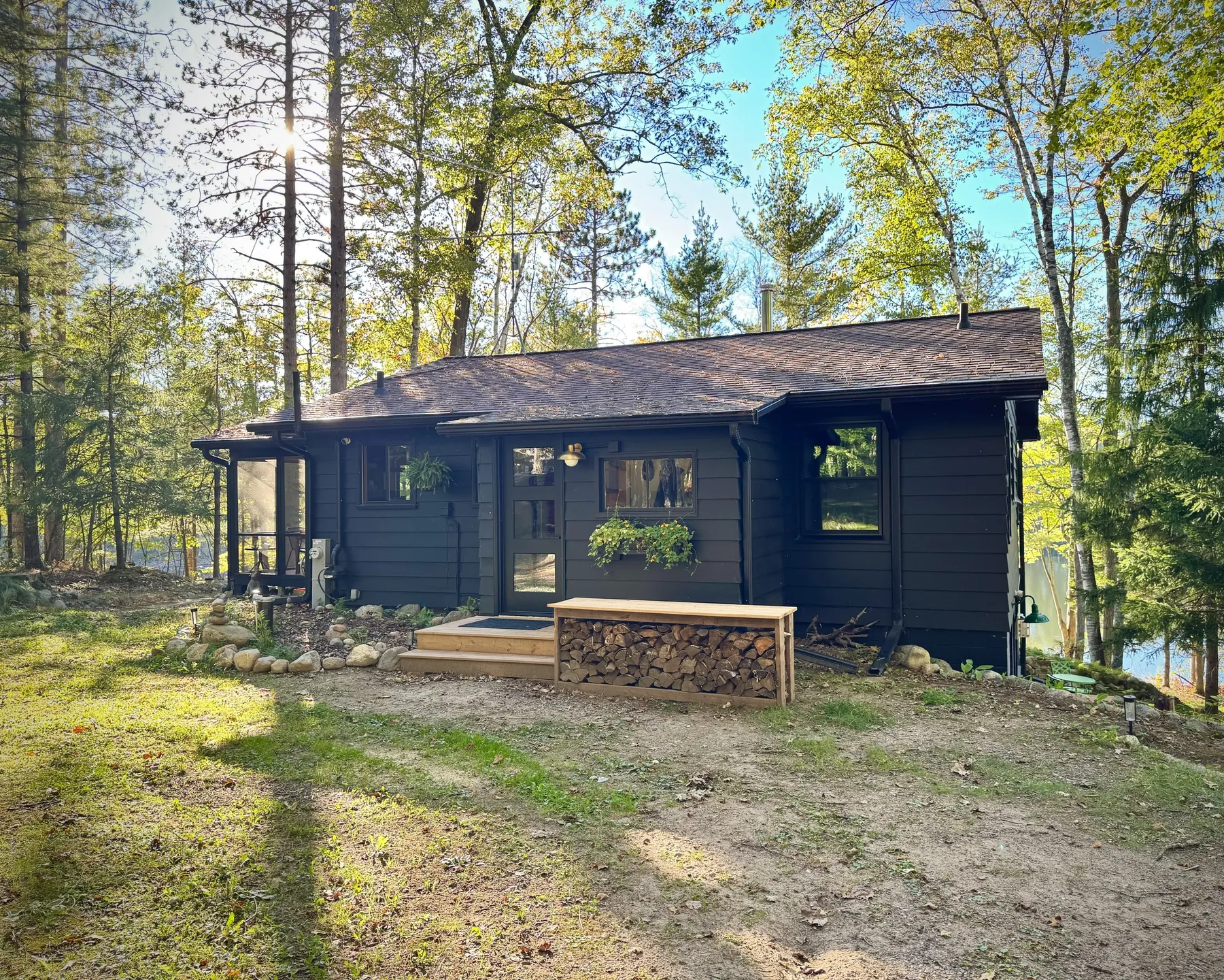 Cabin front after the remodel, dark siding, new black door, wood steps and firewood bench