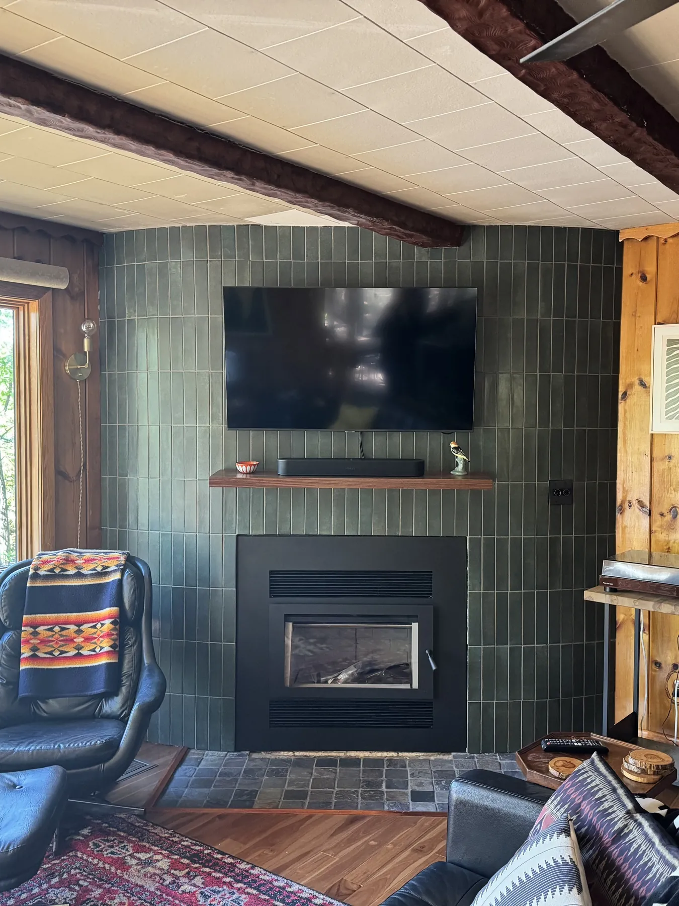 Fireplace wall after the remodel, dark green tile with a wood mantel