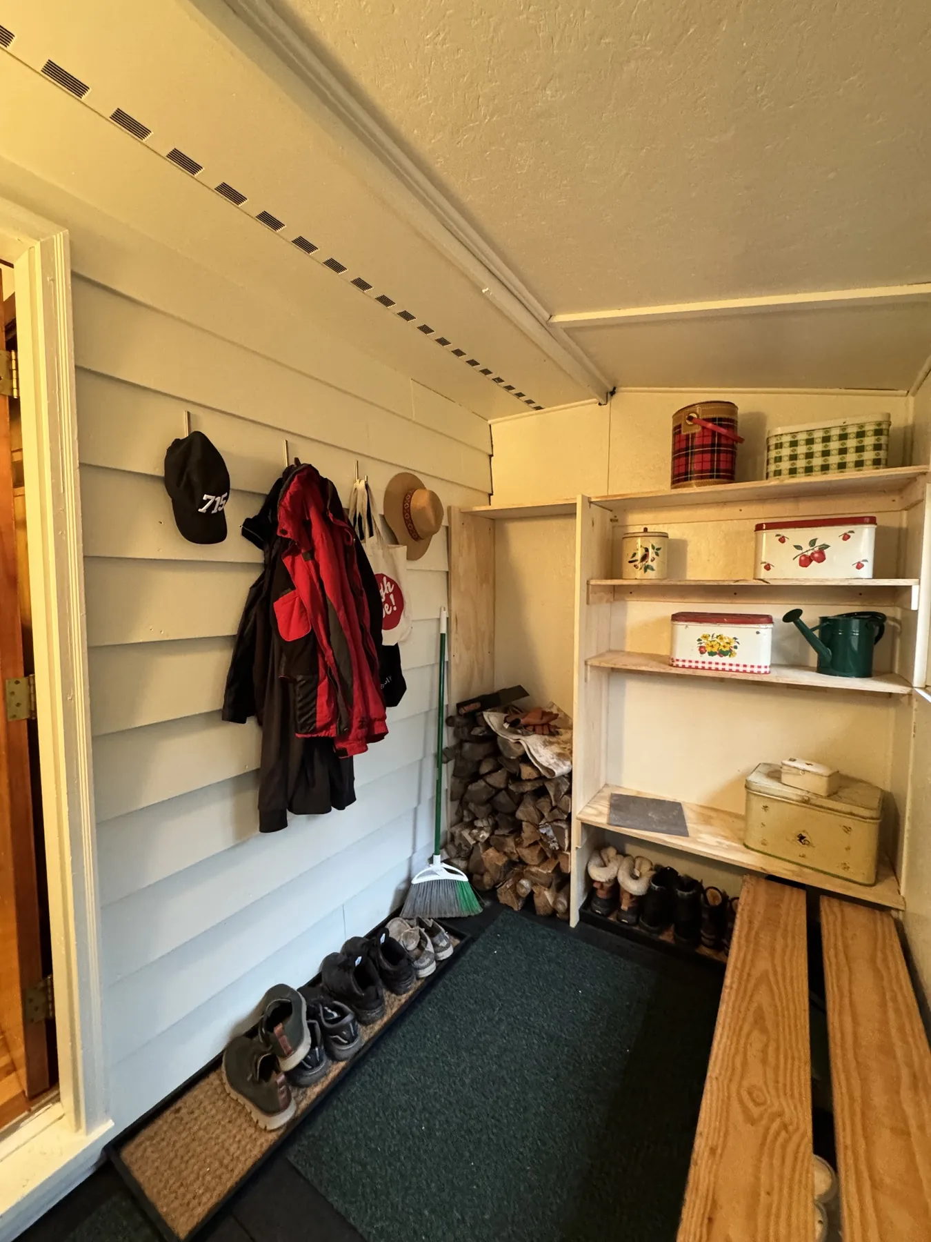 Entry mudroom after the remodel, white walls, wood bench, shelves and a green runner