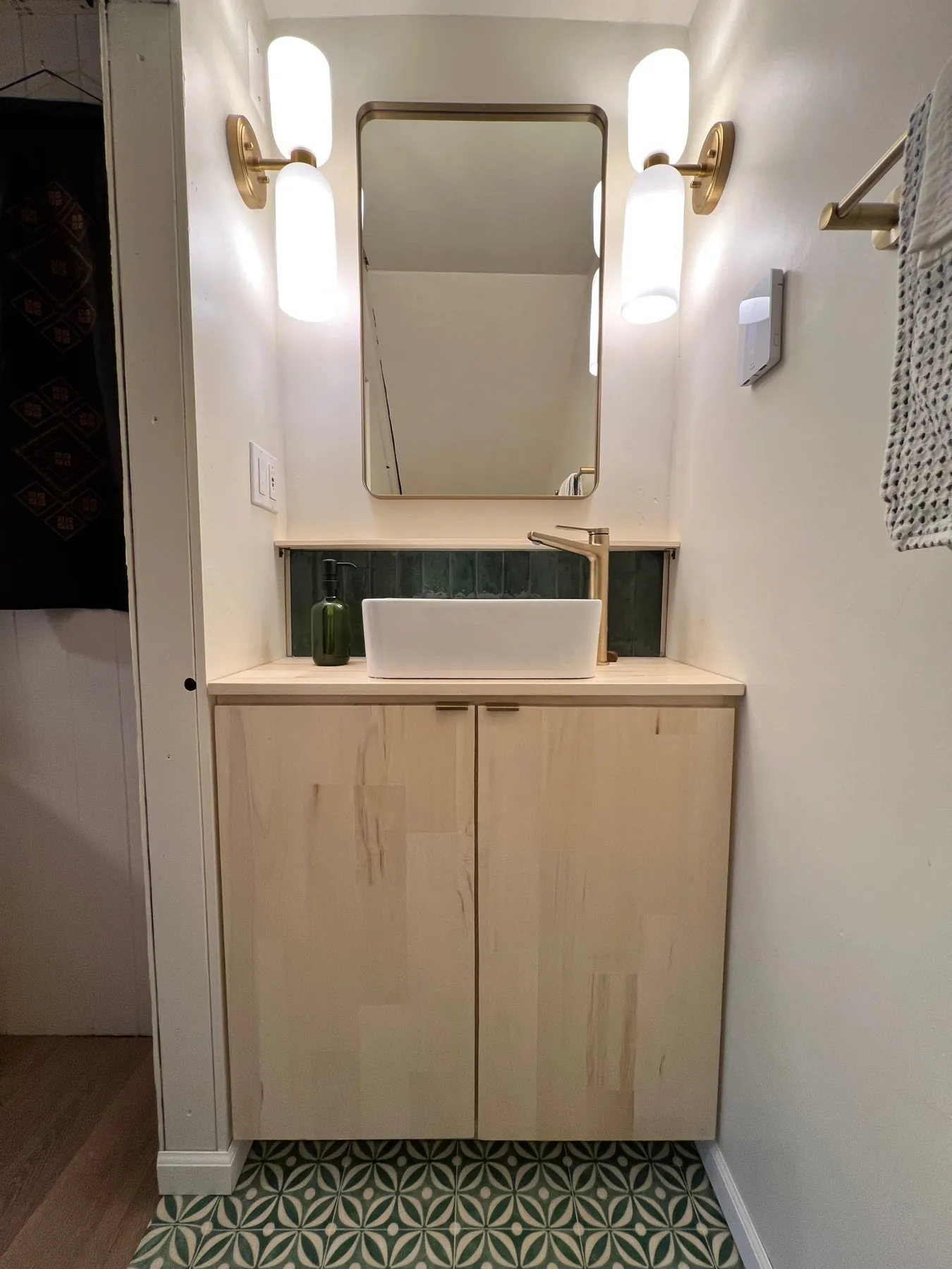 Small bathroom with a birch vanity, brass fixtures and green patterned floor tile