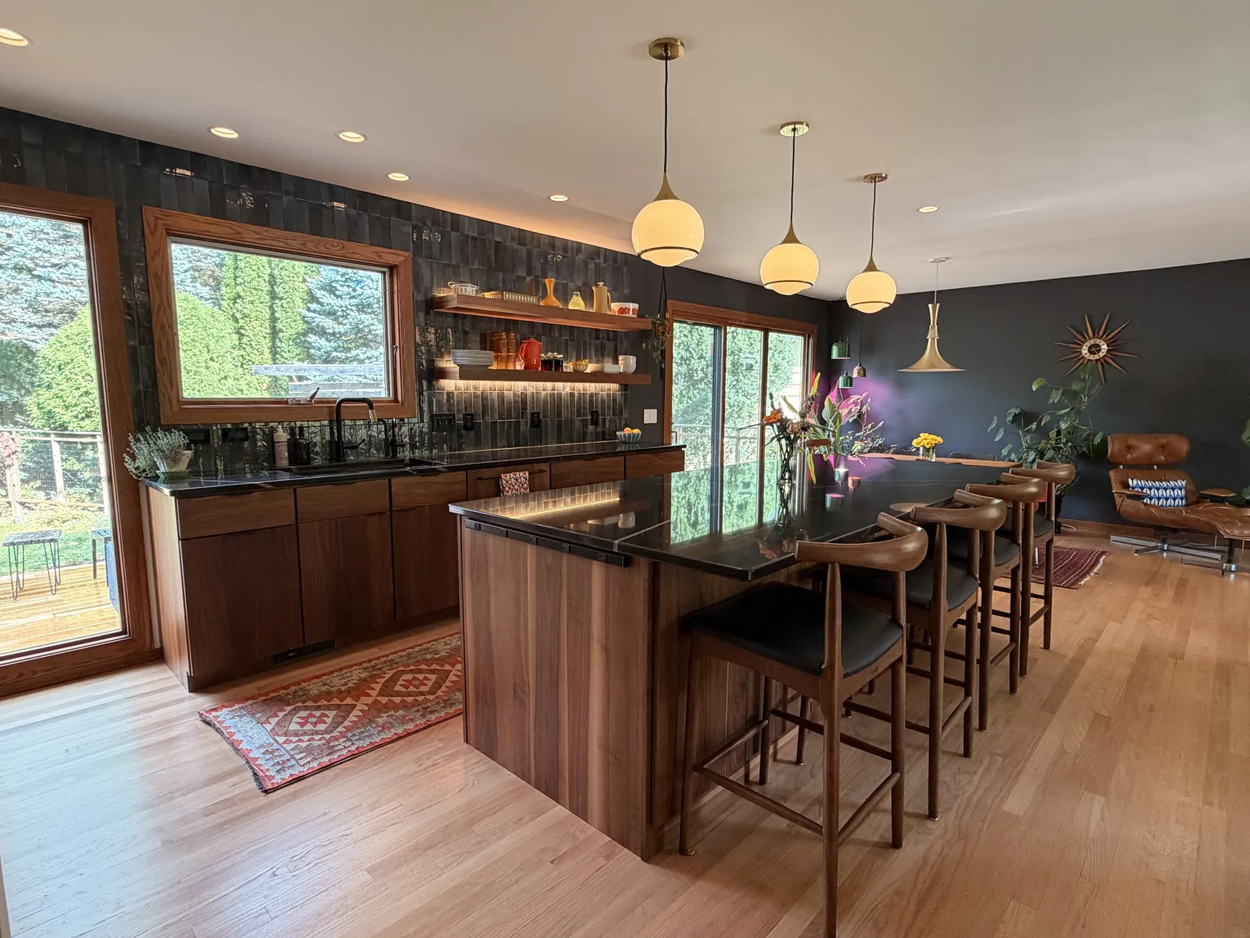 Remodeled kitchen with walnut cabinets, a dark stone island, globe pendants and large windows
